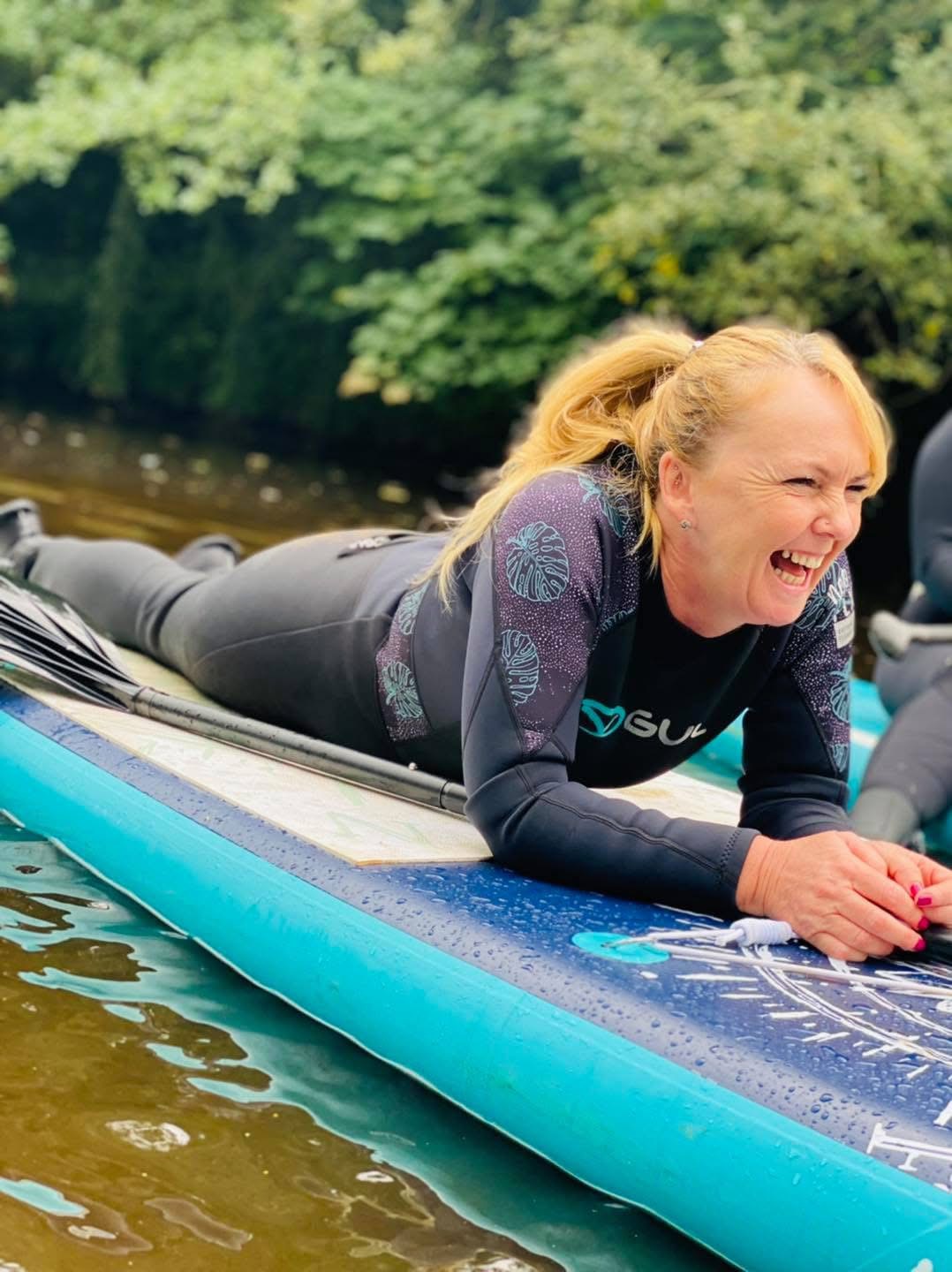 Laughing paddle boarder lying on a board on the river