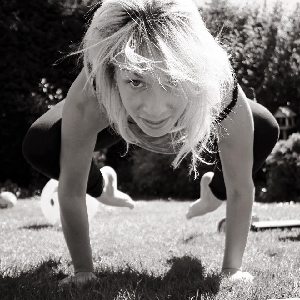 Crow pose held on sunlit grass, hair loose in the breeze
